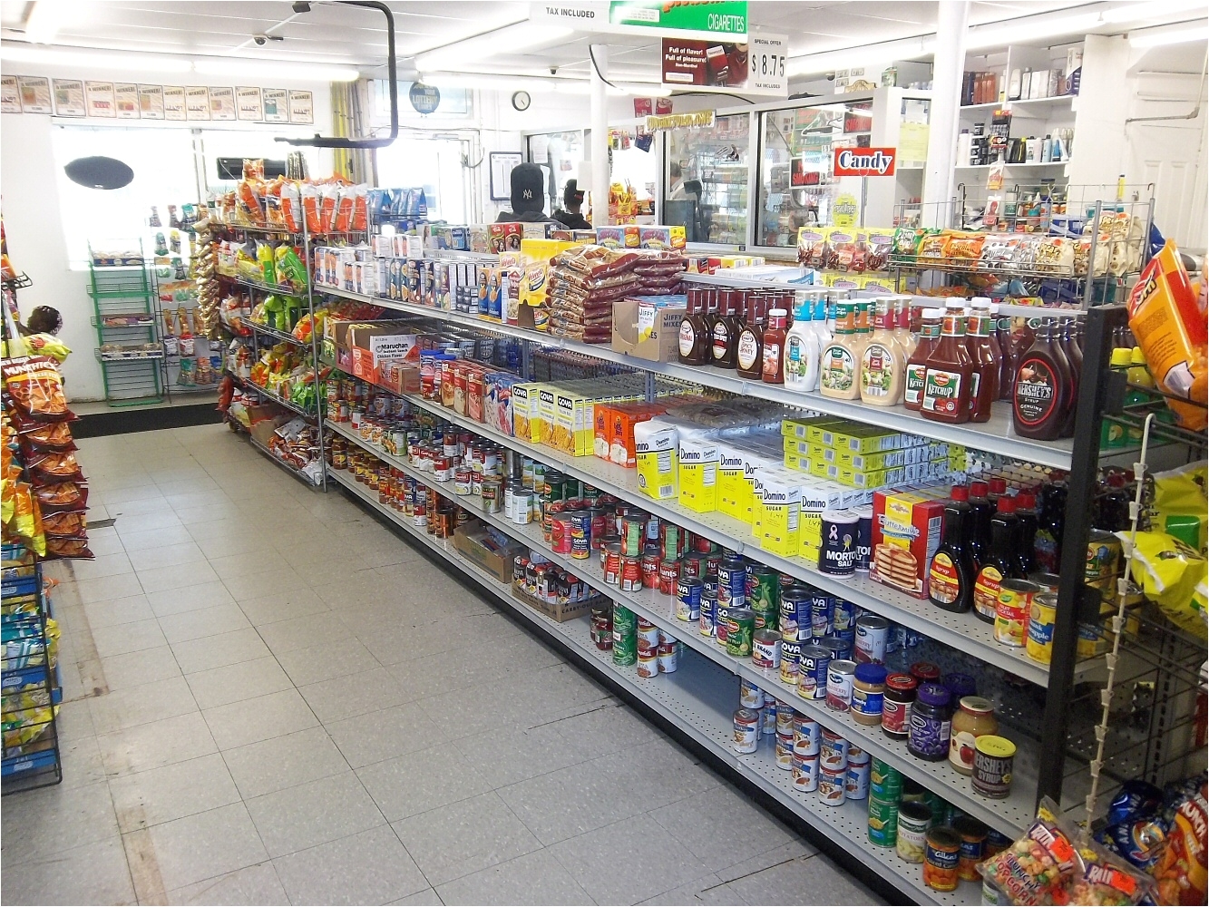 across the iasle are shelves loaded with can goods sugar and salt condiments rice and pasta