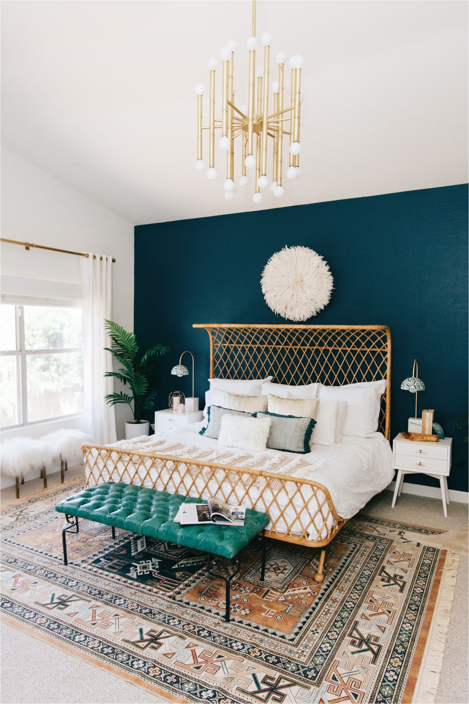 rattan king size bed against a teal wall with a boho rug and teal tufted leather bench makes for a cozy and eclectic master bedroom