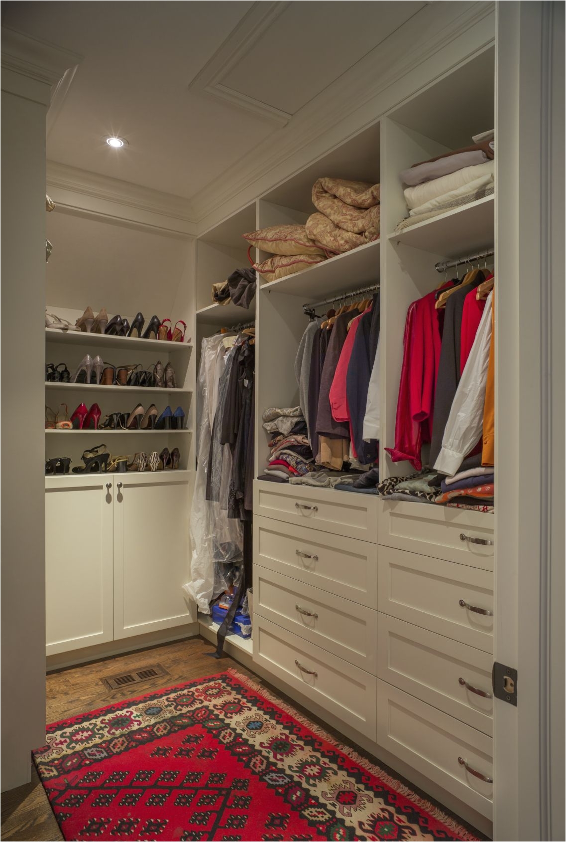 this walk in closet is on the smaller side with white storage drawers and shoe racks the bold red rug covering the dark oak hardwood flooring warms up the