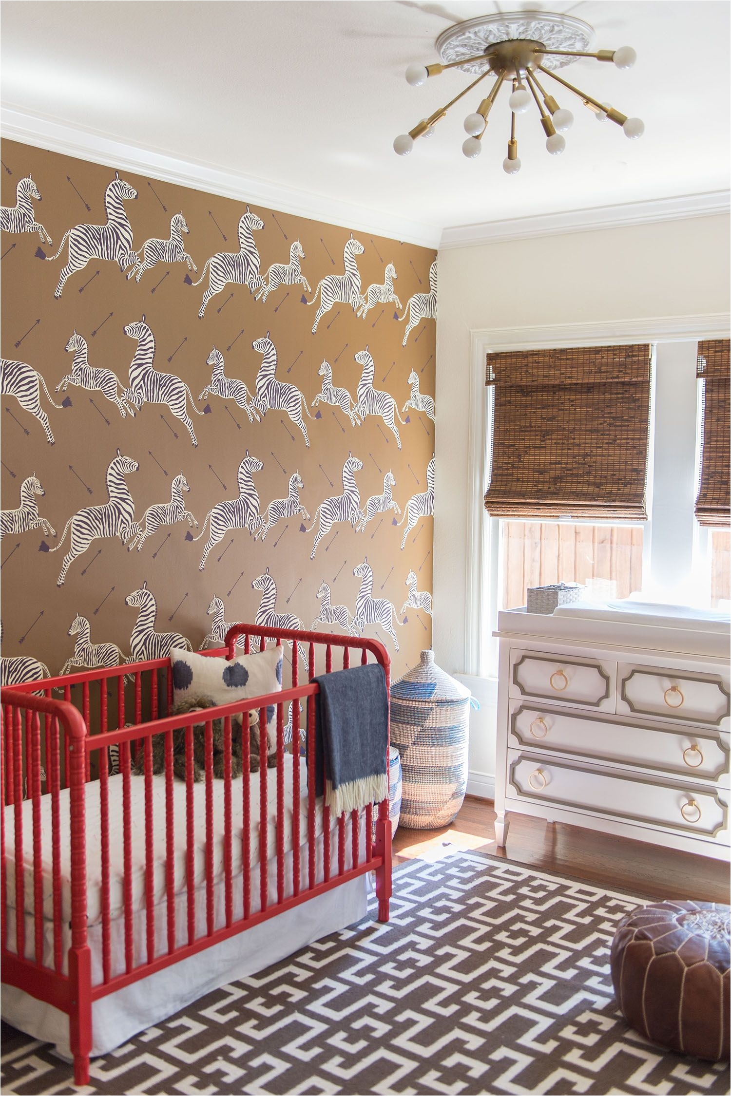 zebra wallpaper in nursery with gold light fixture and red crib