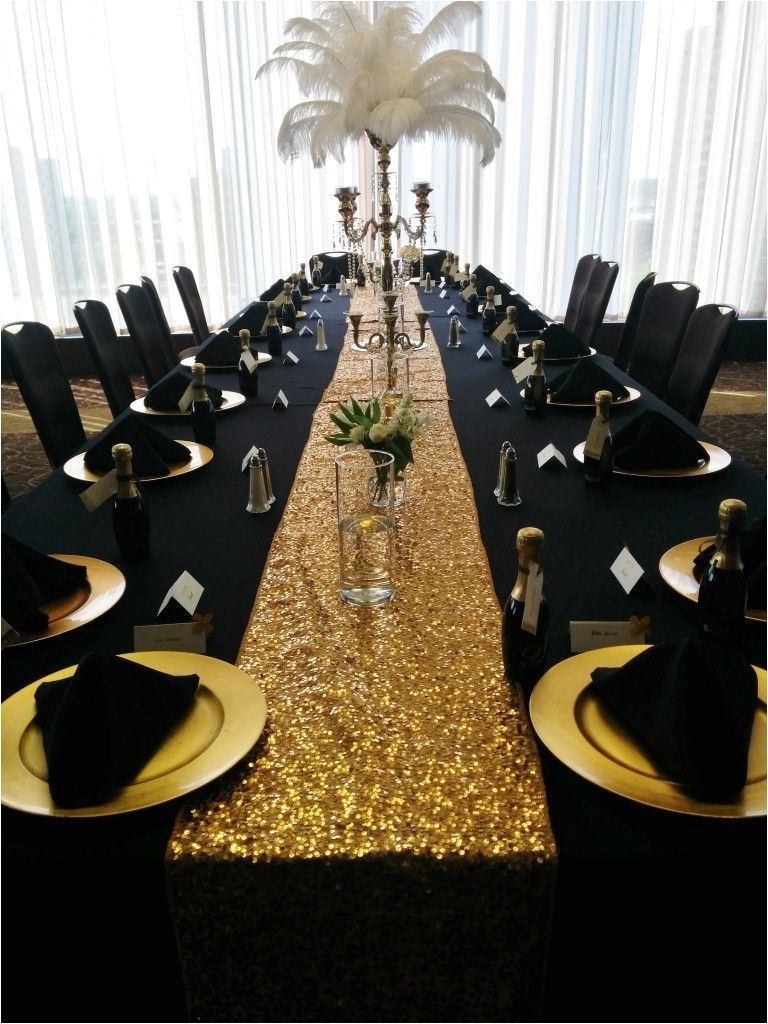 black table linens gold charger plates black napkins pyramid fold gold sequin runner small floral in vase large gold candelabra with peacock feathers