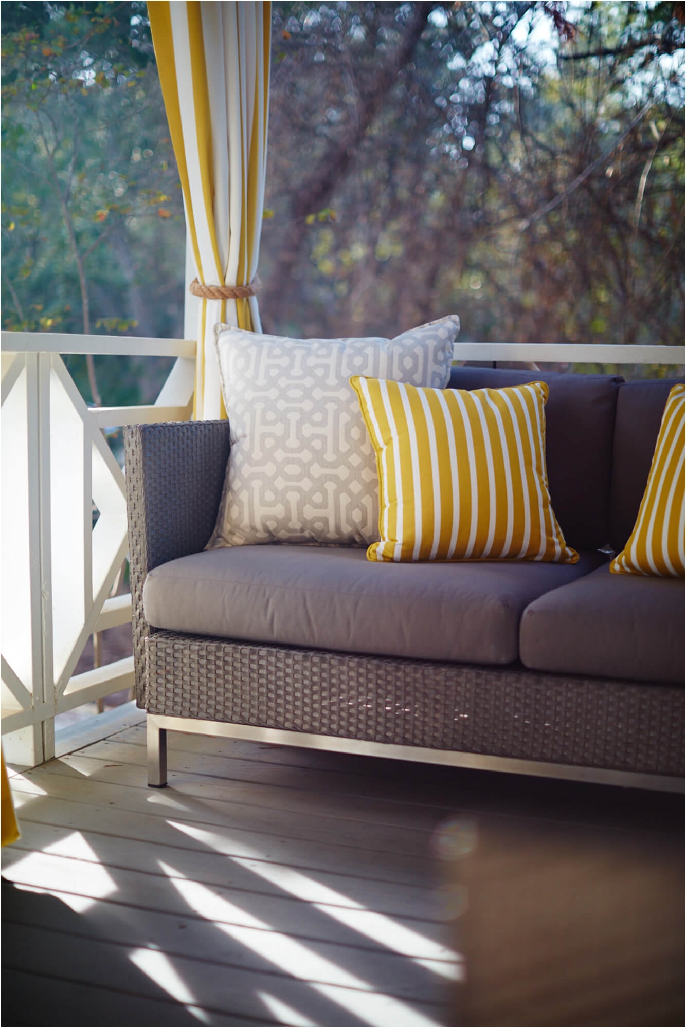 outdoor sofa with yellow and grey decorative throw pillows and yellow and white striped drapery