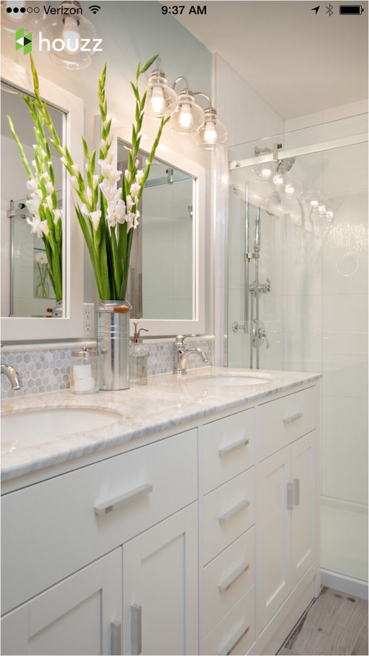small bathroom with white cabinets under two white sinks white wooden framed mirrors white ceramic tiles wall in the shower area with glass partition
