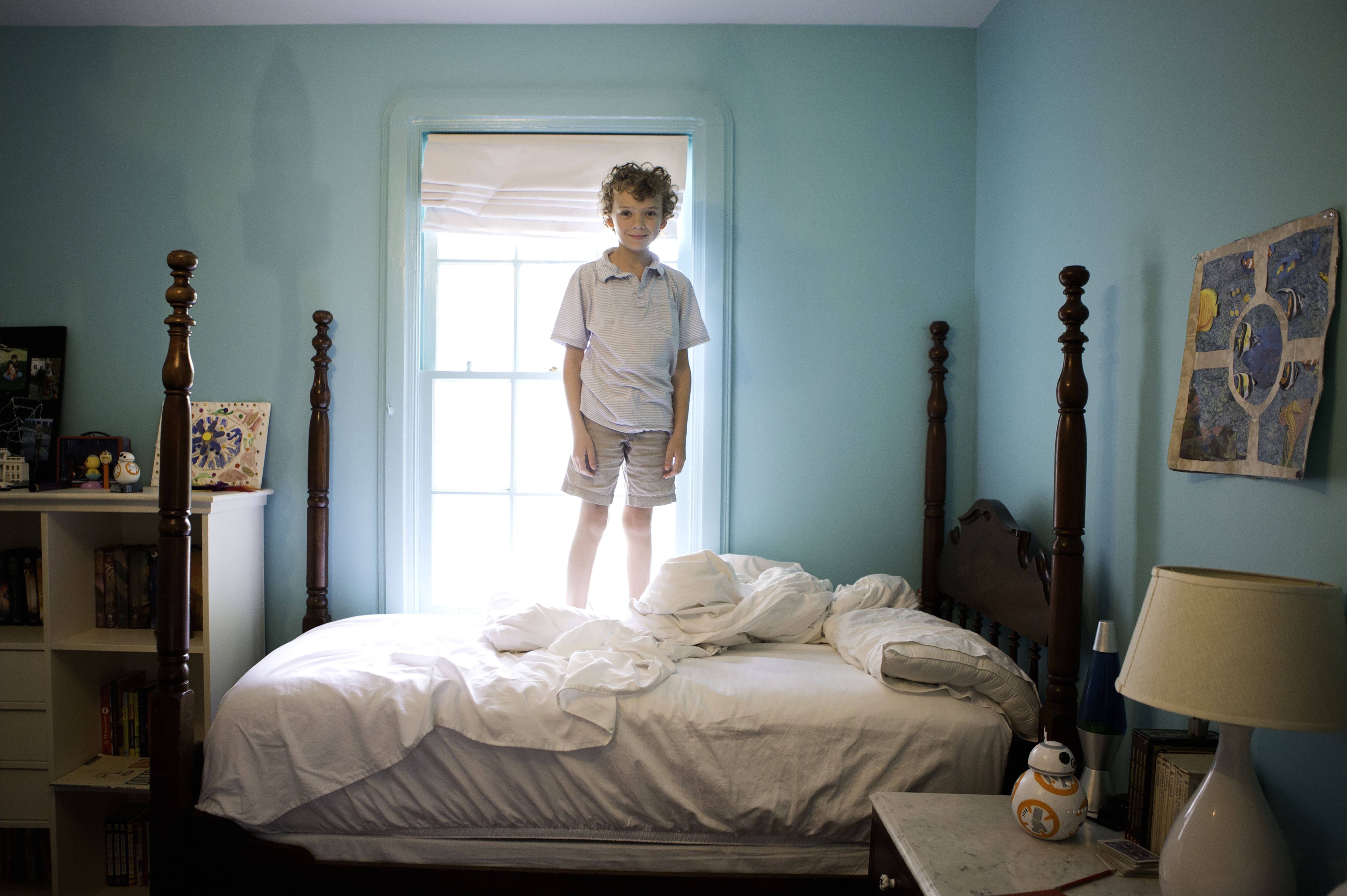 young boy standing on unmade 4 poster bed backlit 5a6a f4e b53c2