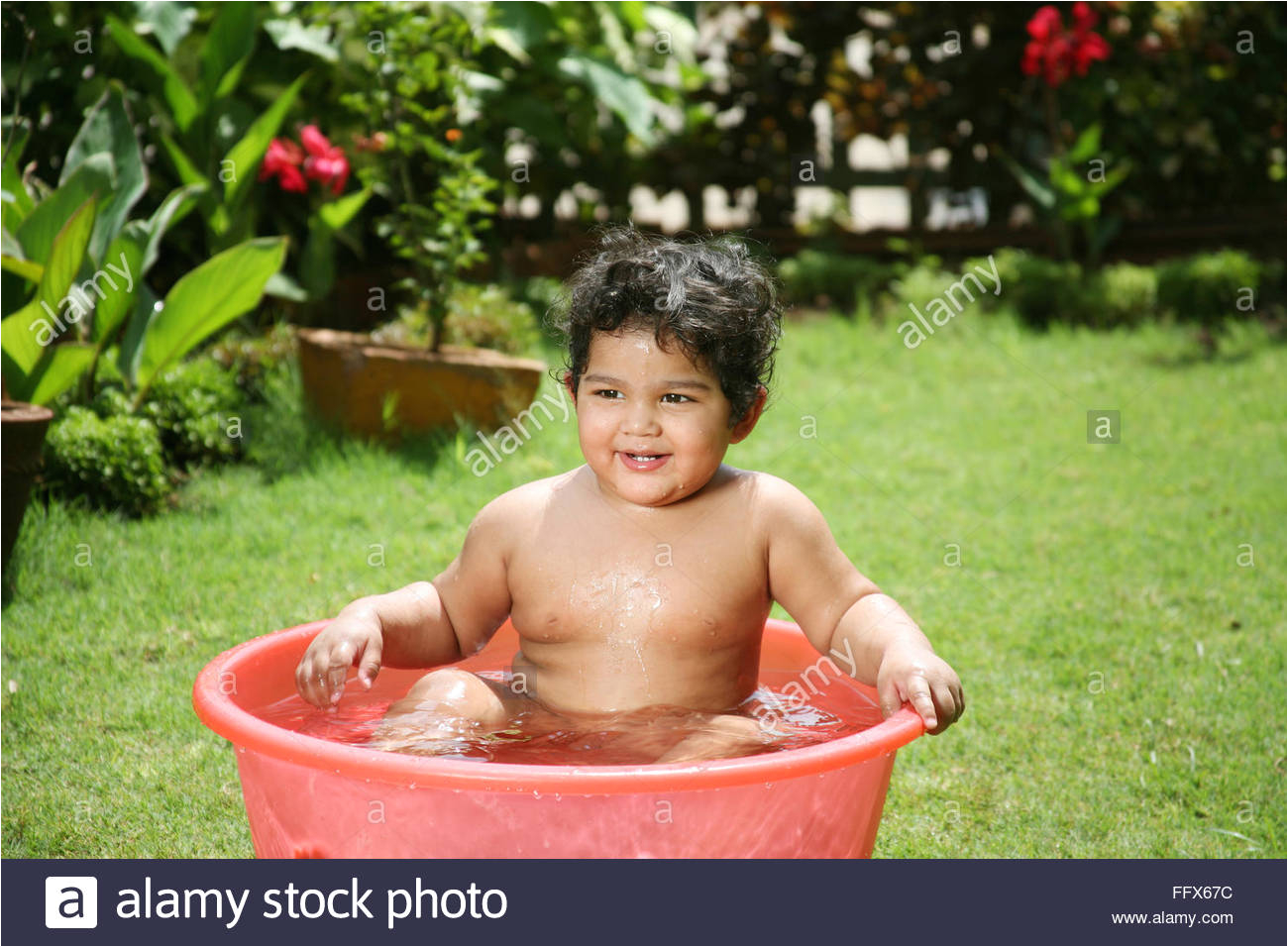 stock photo one and half year old baby sitting in red plastic tub with water and